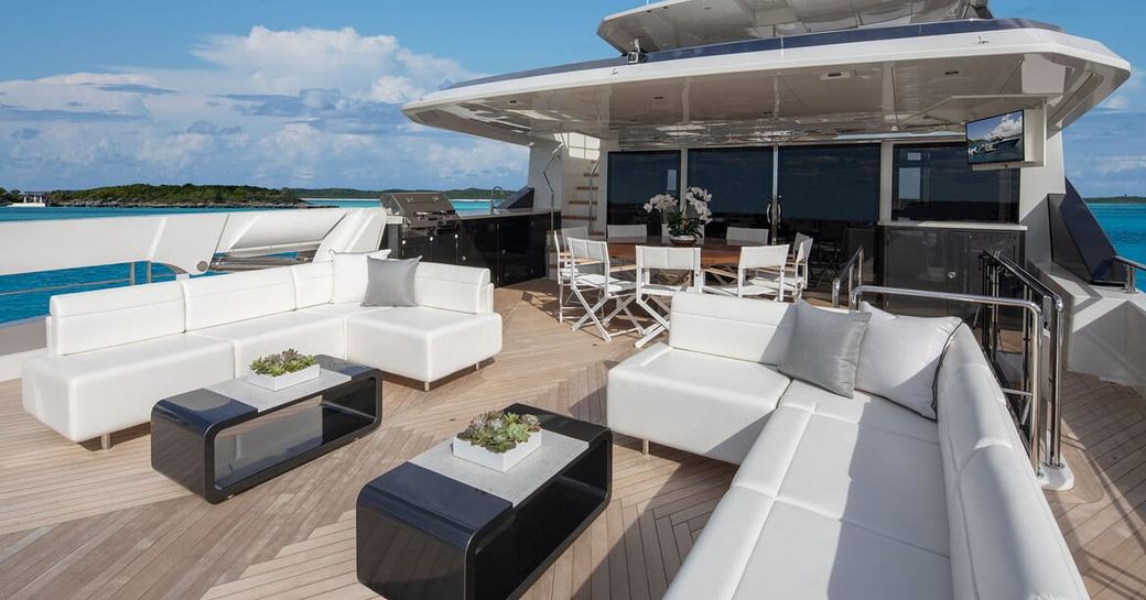Overview of the aft deck onboard charter yacht ENTREPRENEUR, alfresco lounge area with facing L-shaped white sofas and black coffee tables