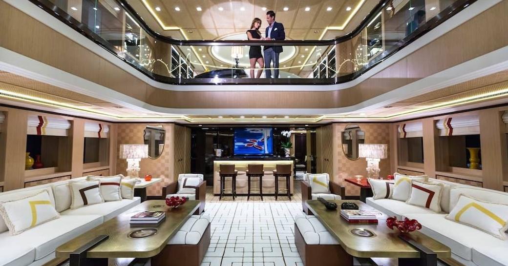 charter guest stands on balcony overlooking main salon on board superyacht AXIOMA 