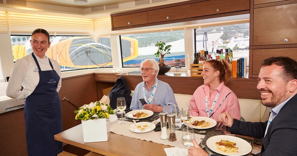 A superyacht chef presenting a dish to three judges around a table