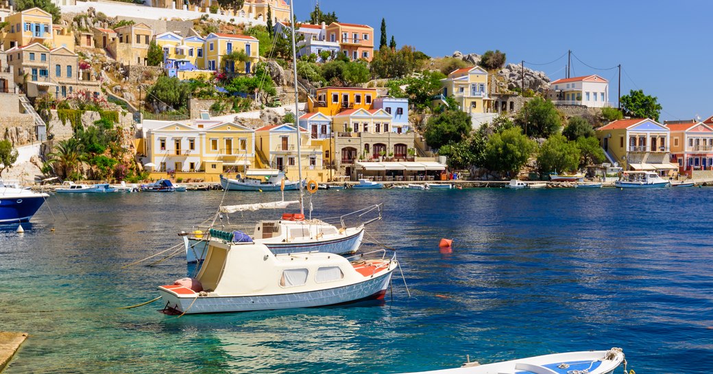 island in greece with little boats on the blue water and pretty town as backdrop