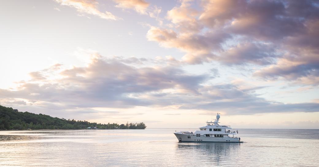 Small motor yacht at anchor in the island of Moorea during a charter trip in the remote islands of French Polynesia, with pink sunset light