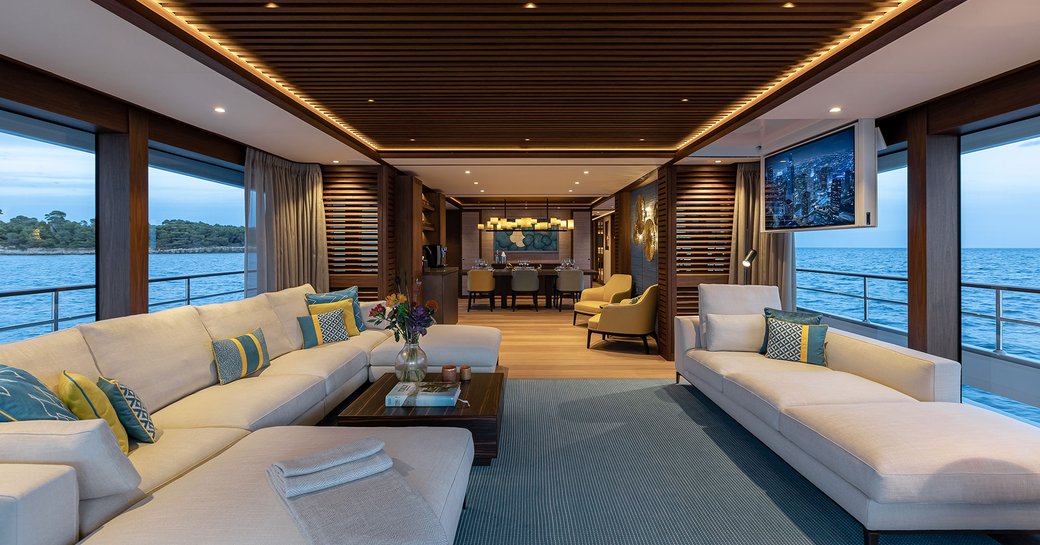 Main salon onboard charter yacht MANA I, spacious lounge with white seating in the foreground surrounded by large windows