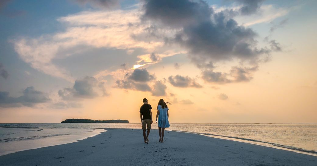 couple holding hands walking towards maldives sunset