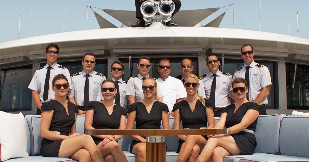 Crew on board a superyacht posing for a group photo on the bridge deck in their formal charter uniform
