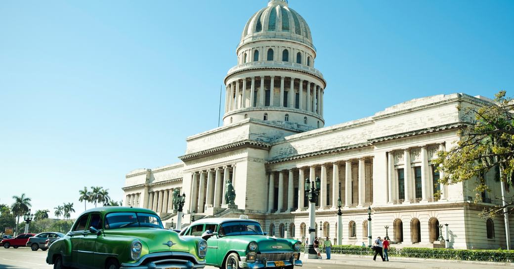 vintage cars cruise through the streets of Cuba lined with colonial architecture including the library