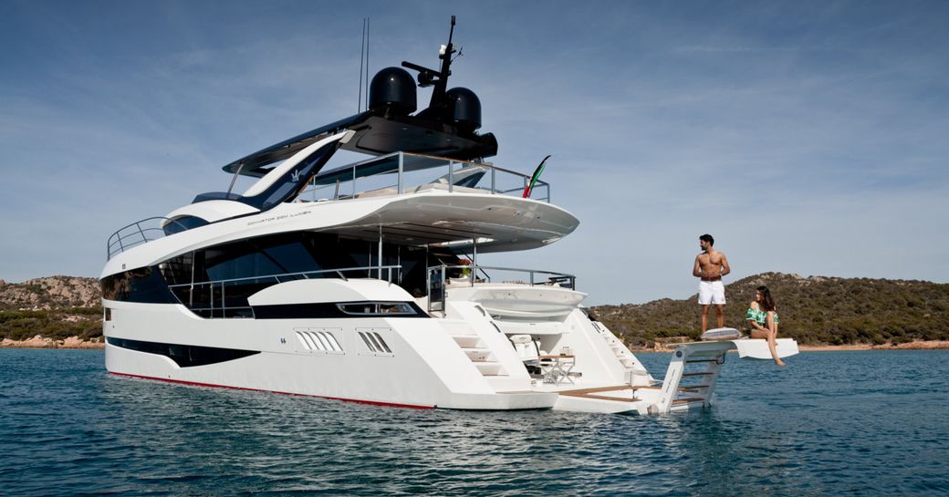 man and woman sit on extendable swim platform of luxury yacht hanaa, looking at yacht