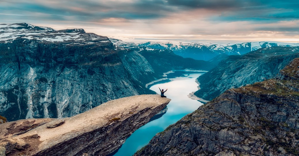 man sits on the edge of the Trolltunga rock looking over fjord in Norway