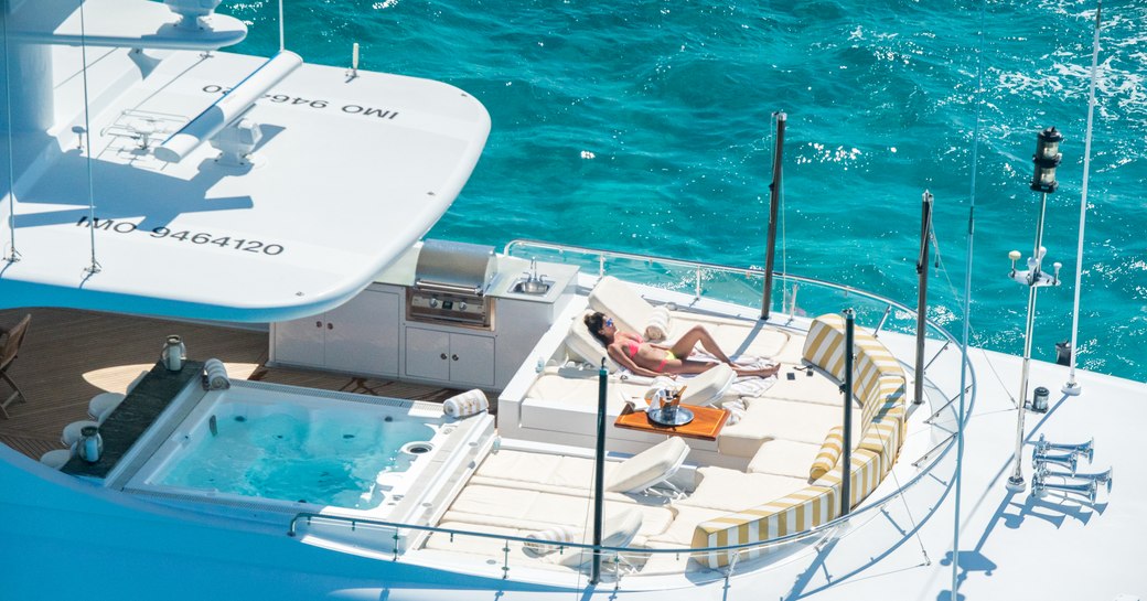 A charter guests sunbathes on the foredeck of a superyacht close to a Jacuzzi