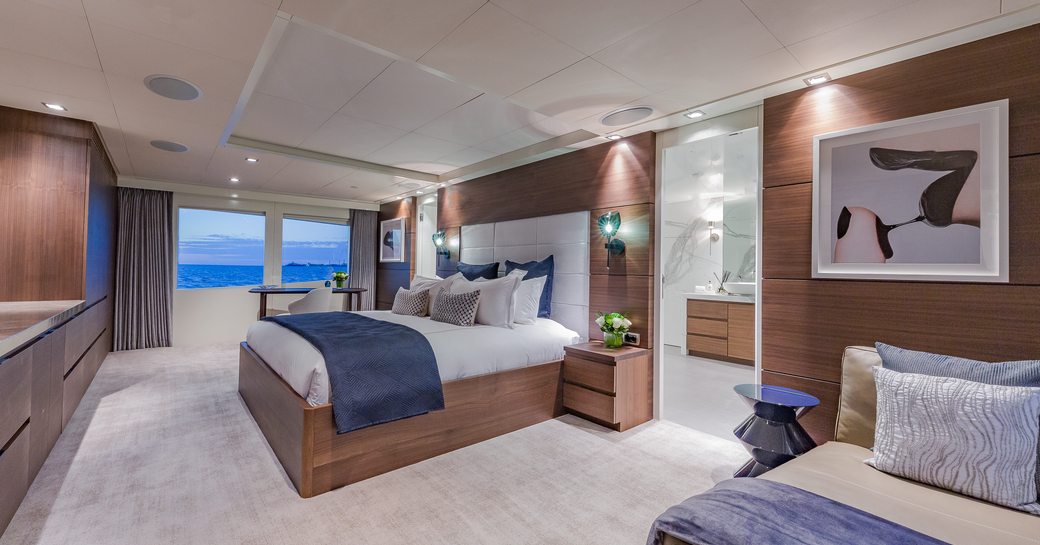 Master cabin onboard charter yacht BIG SKY, central berth facing port with large windows in the background and seating area in the foreground