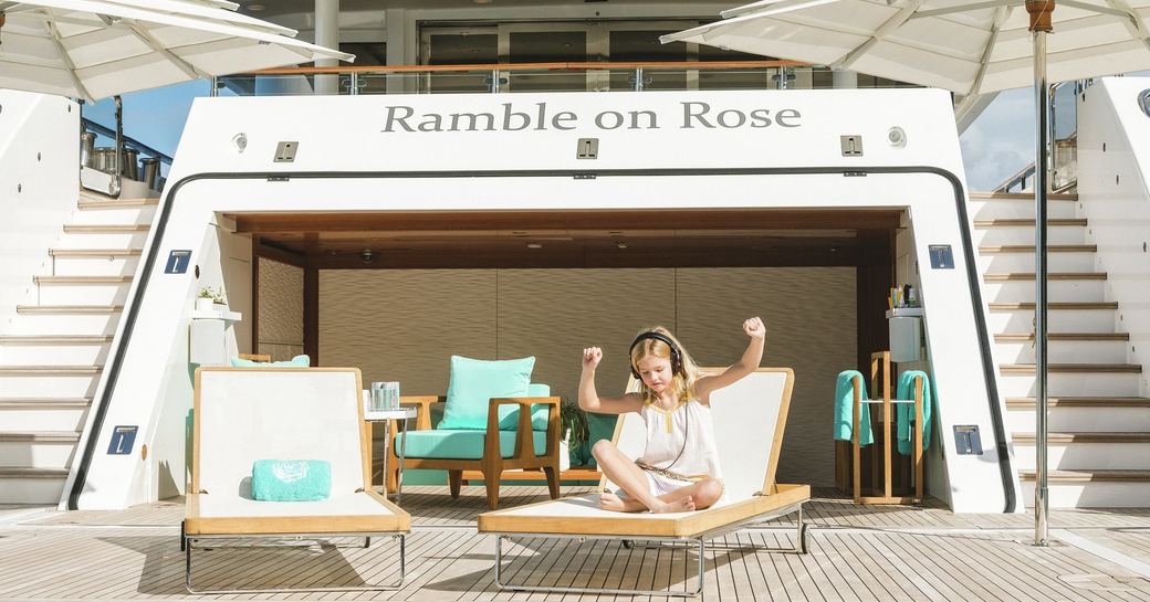 child listens to music while sitting on a sun lounger on the swim platform of charter yacht Ramble on Rose 