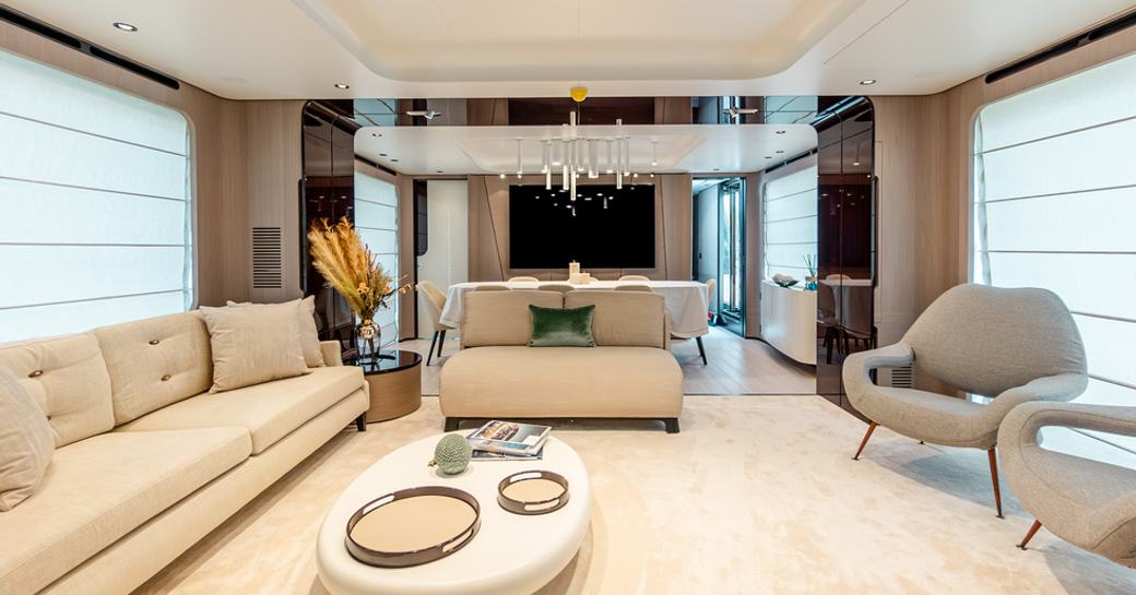 Overview of the main salon onboard charter yacht VESTA, spacious lounge area with cream sofa to port and gray armchairs starboard