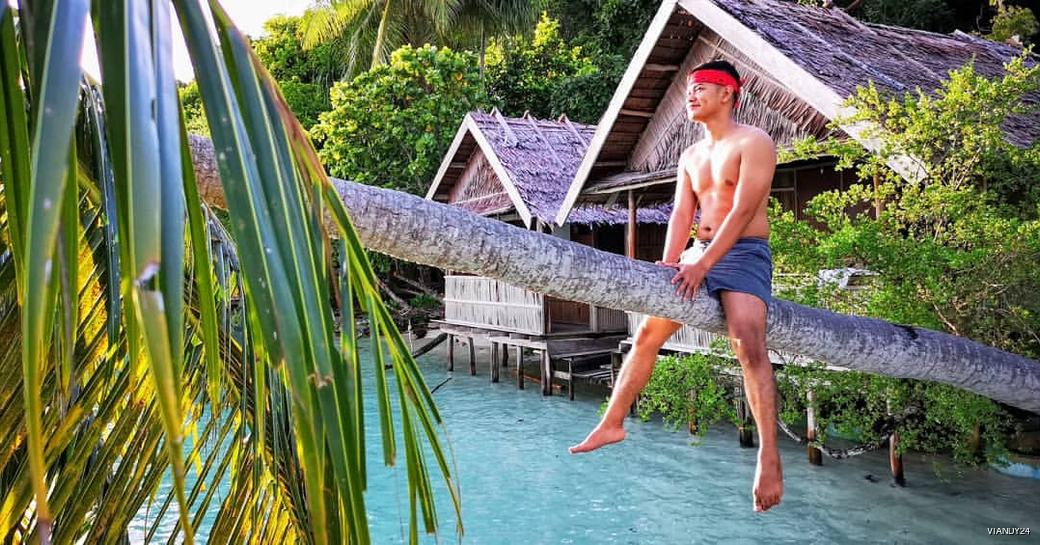 Man sat on tree trunk hanging over the water by local homestays 