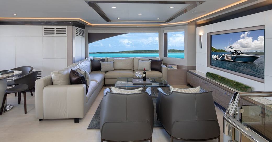 Overview of the main salon onboard charter yacht ENTREPRENEUR, lounge area with large wall mounted TV and big windows in the background offering views of the sea.