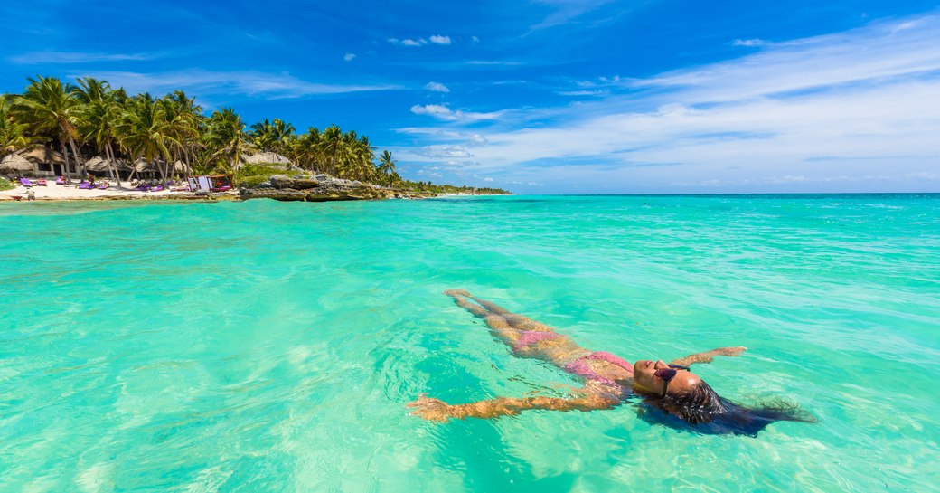 woman floats on surface of caribbean sea with island in background