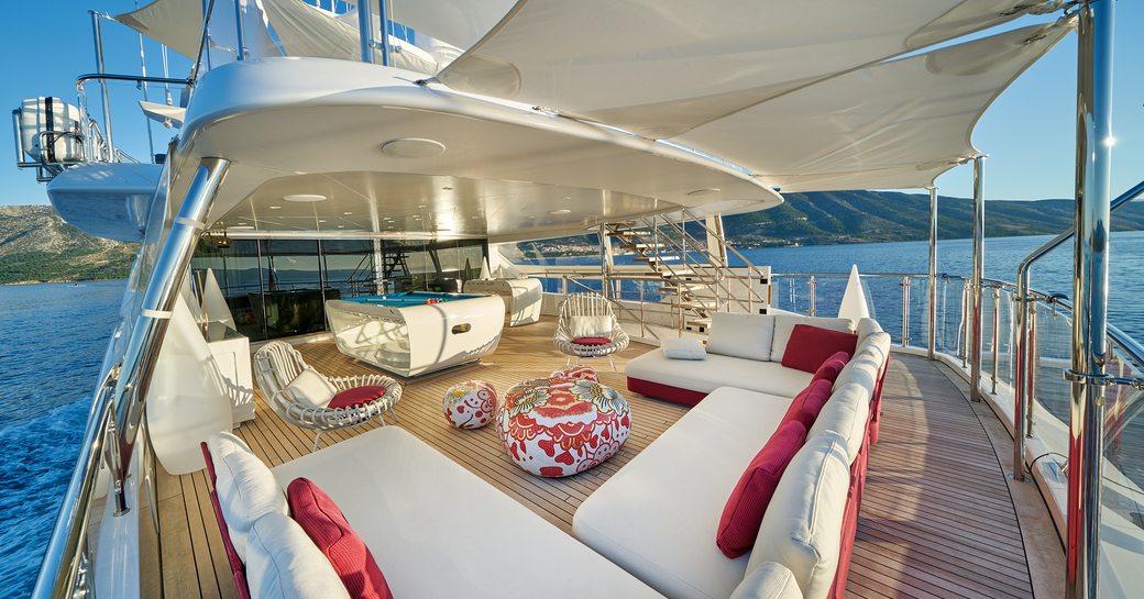 Exterior deck space onboard charter yacht HAPPY ME, biminis cover seating area with white seats and red cushions