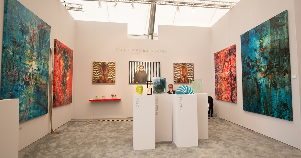 Painting gallery at Art Basel Miami, small room with all walls lined with paintings, plus handful of podiums with small sculptures