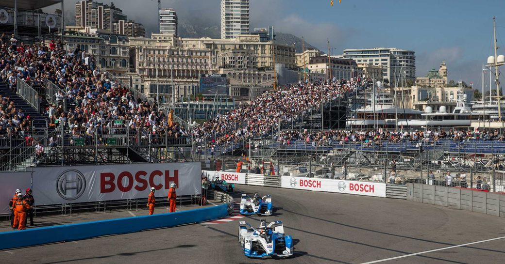 Two racers speeding round track at Monaco E-Prix, surrounded by stands of spectators.