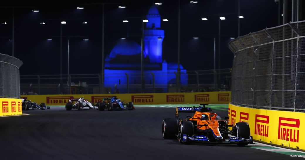 Ground level view of Jeddah Corniche Circuit with racers on the track and a mosque in the background at night.