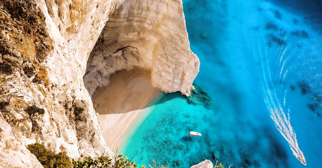aerial shot of small cove in greece, with yacht on the water and sandy beach and caves