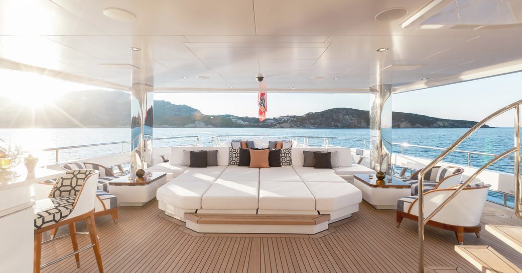 view of main deck aft on board feadship luxury yacht joy, with sun pads in centre and wet bar to the right and caribbean ocean in background