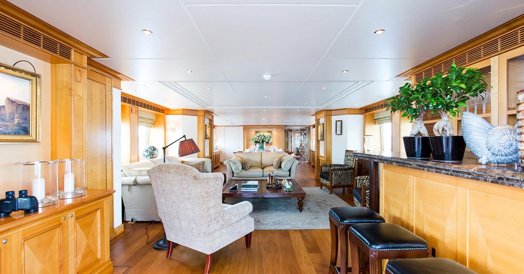 cherrywood panelled main salon of superyacht ‘Seven Sins’ with marble-topped bar and sumptuous lounge