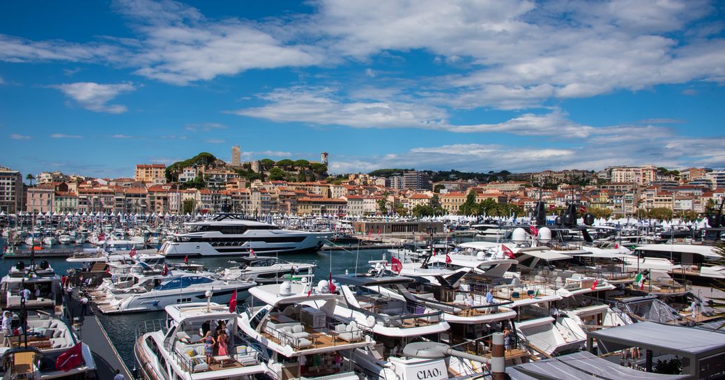 Overview of Vieux Port in Cannes. Many motor yachts berthed in marina with Cannes visible in background. 