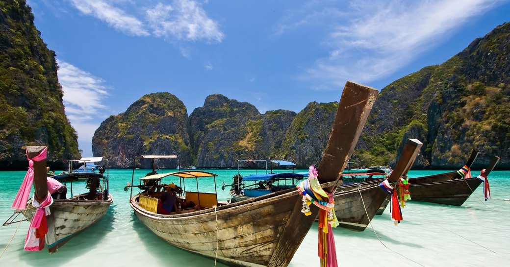traditional Thai fishing boats line up on the white sandy shores of Maya Beach on Koh Phi Phi, Thailand
