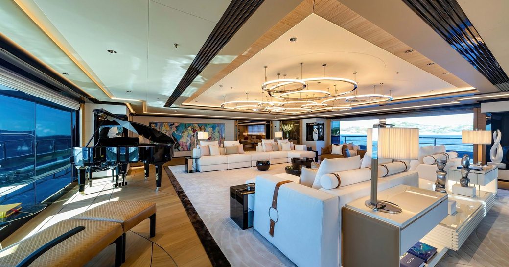 Overview of the main salon onboard charter yacht PROJECT X, spacious lounge area forward and a grand piano in the background