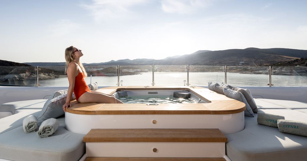 emale sitting on edge of Jacuzzi on superyacht O'PARI in the sun with coastline behind