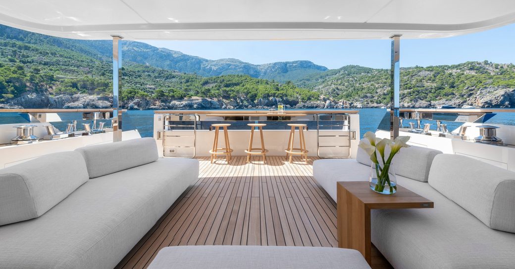 Deck of SANGHA superyacht, light colored sofas, teak decking and hills in the background