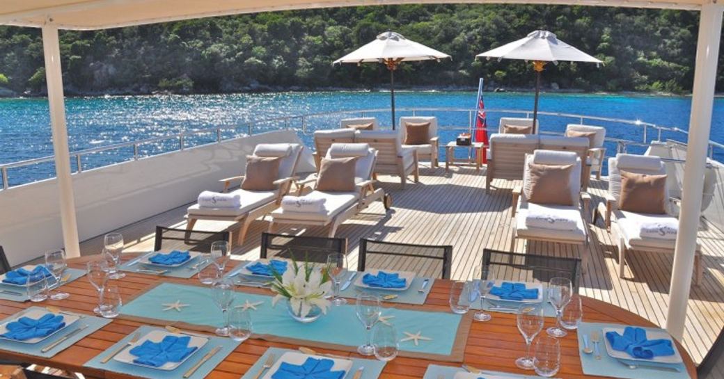 Sunbathing area on the aft deck of a luxury yacht, with sunloungers and dining set-up