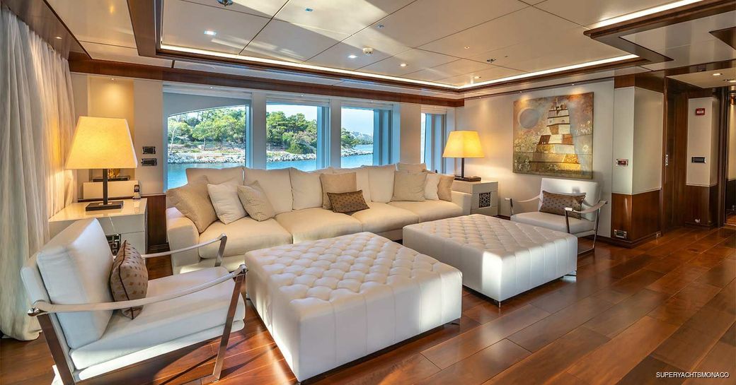 Main deck lounge area onboard M/Y IMMERSIVE, white sofas and armchairs facing toward each other with large window in the background.