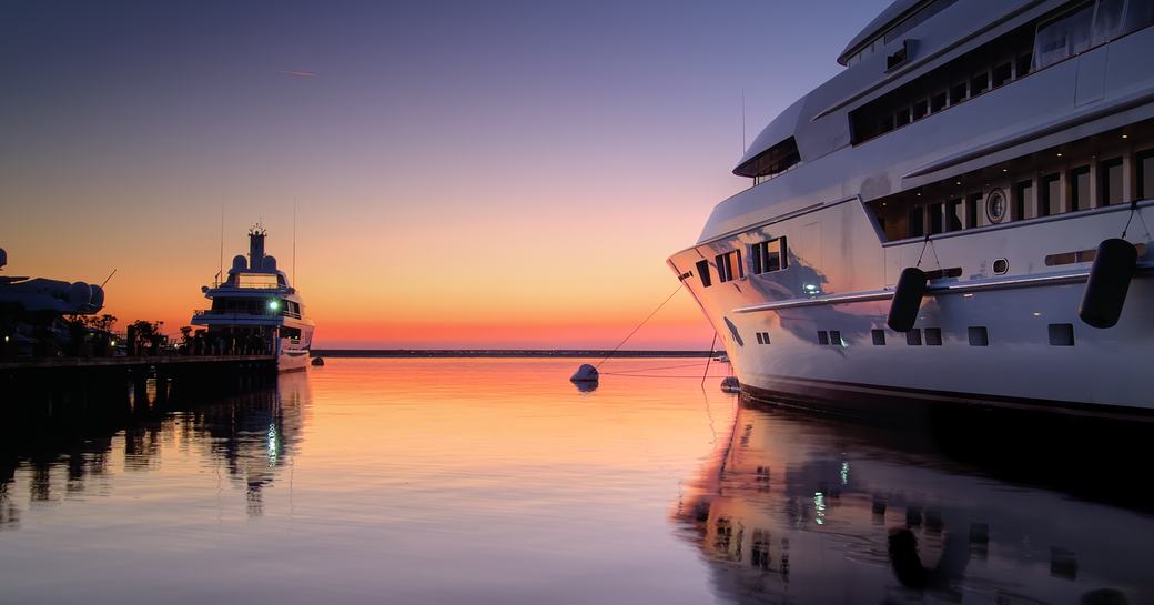 The port side of a superyacht in a marina at sunset