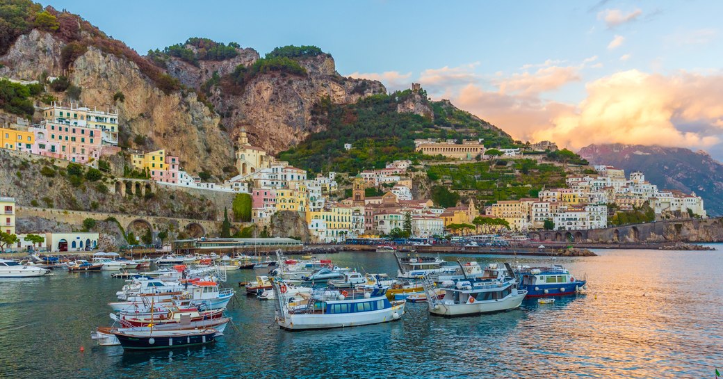 View of harbour in Italy with fishing boats and dramatic coastal scenery in background