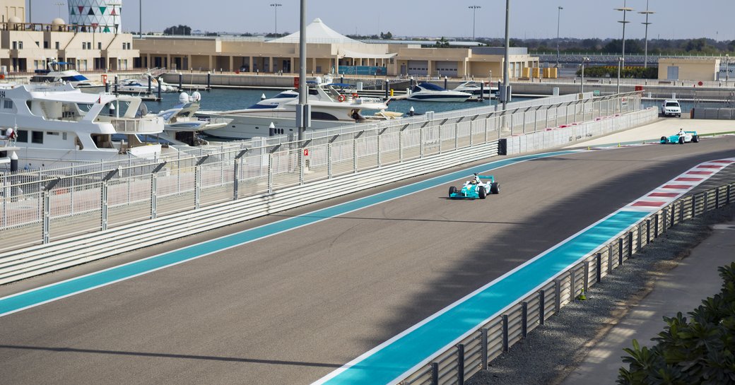 Formula 1 racer on Abu Dhabi Yas Marina Circuit, motor yachts berthed adjacent to track.