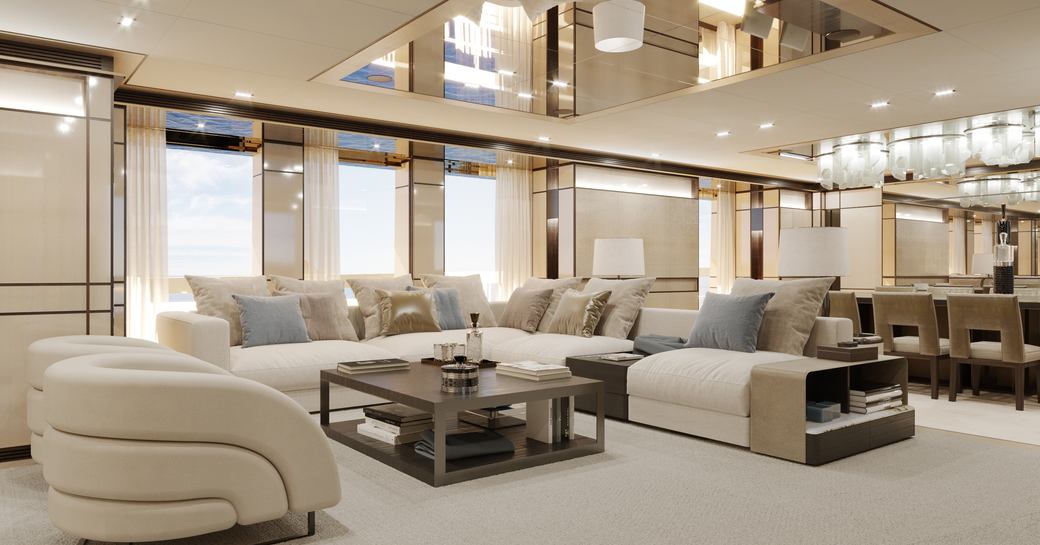 Overview of the main salon onboard charter yacht RELIANCE, lounge area facing in toward a coffee table with a dining area aft and large windows surrounding.