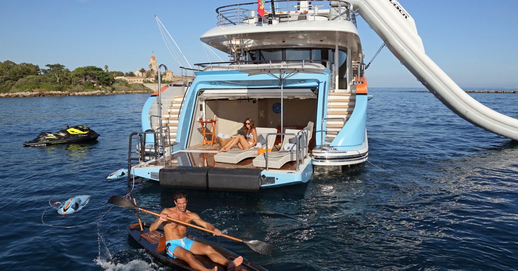 Man and woman enjoying chartering in Italy on motor yacht AURELIA, with woman sitting in beach club and man using the kayak