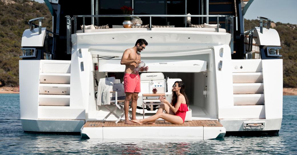 man and woman sit on swim platform of luxury yacht from dominator ilumen series