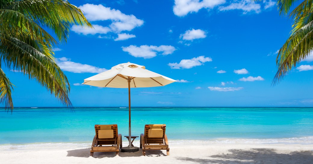Two Sunloungers on a white sandy beach looking out onto clear blue waters in the Caribbean