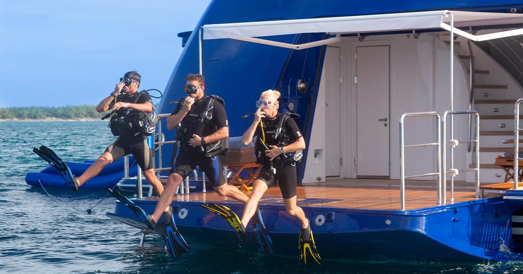three guests on luxury yacht charter vacation scuba dive in a secluded cove