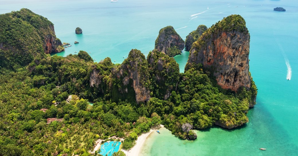 rocky outcrop covered in lush forest in a sheltered thailand bay in turquoise waters