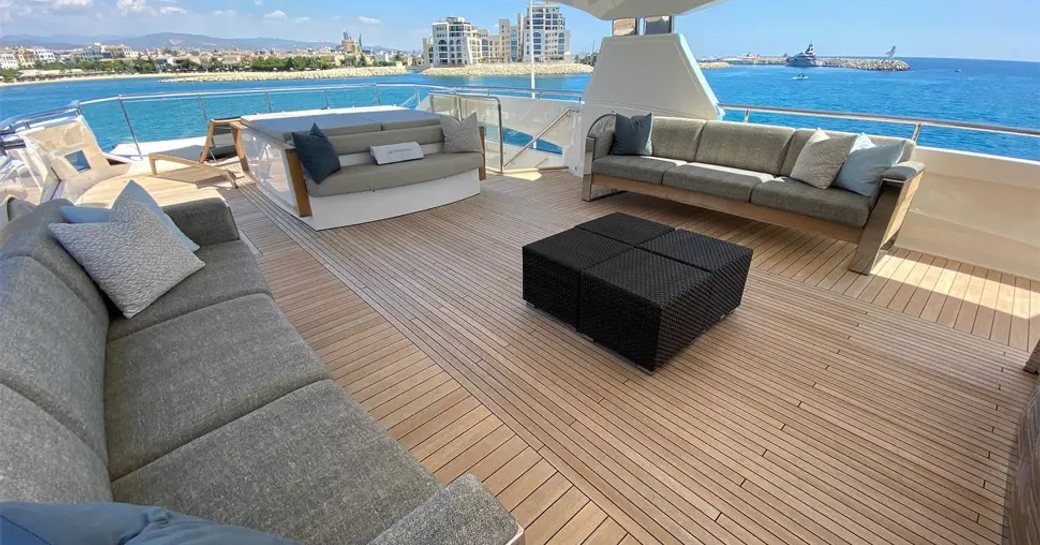Overview of the upper deck aft onboard charter yacht LE VERSEAU, with large gray sofas facing in towards a black coffee table