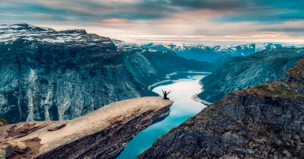 Man sits on on the mountain's cliff edge of Trolltunga throning over Ringedalsvatnet watching the sunset in Norway
