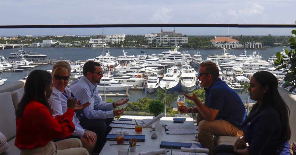 Group of visitors at the Palm Beach International Boat Show having a meeting at a coffee table with views of the marina in the background.