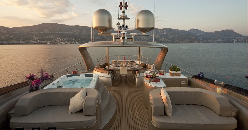 Chairs and Jacuzzi with alfresco dining in background on sundeck of charter yacht Soiree as sun sets