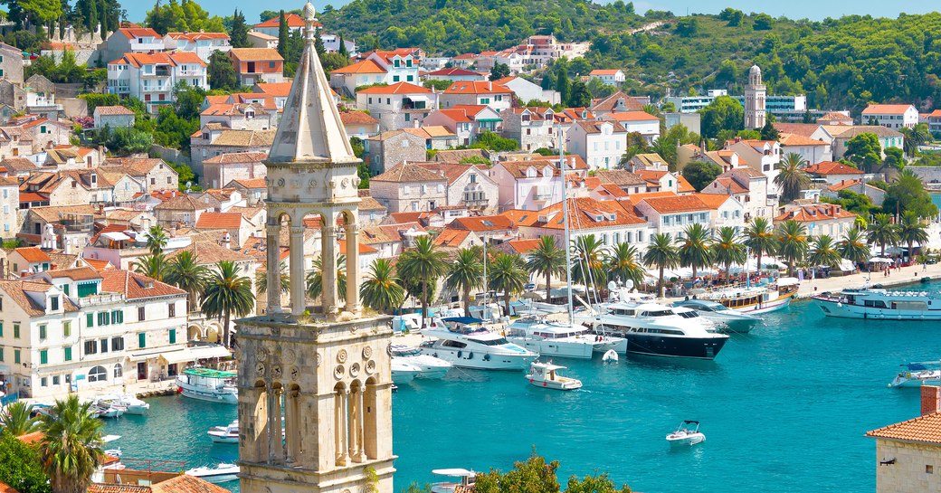 Marina in Croatia with church spire in foreground, and red-roof buildings lined up overlooking bright blue ocean