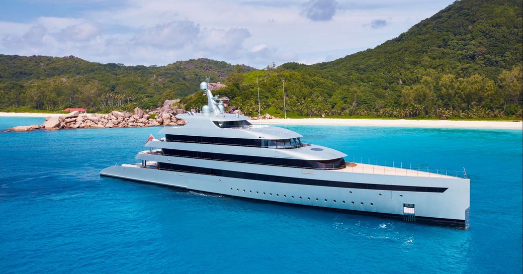 Overview of M/Y SAVANNAH moored in a bay with elevated terrain and a sandy beach.