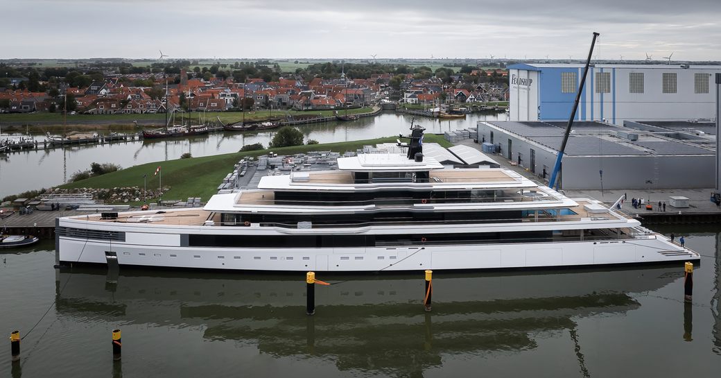 Side view of Feadship Project 1011 following her emergence from the construction shed, with waterways and residential buildings in background
