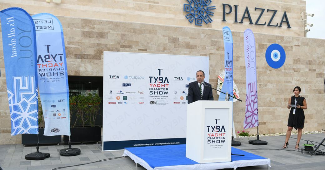 Speaker on stage during TYBA event, surrounded by flags.