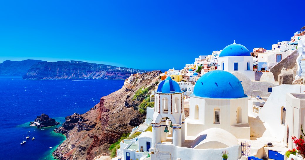 views over the town of santorini in greece, with blue domed roofs and yachts in water